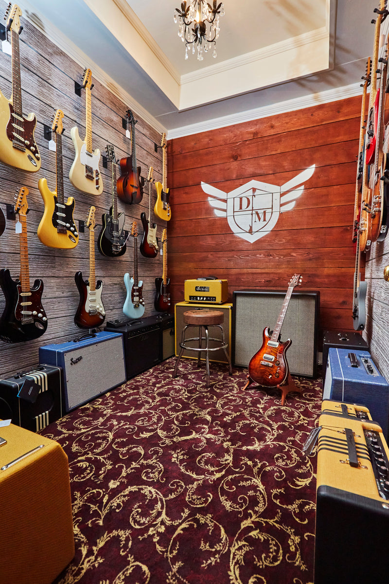 Fender and PRS electric guitars on a barnwood wall above Supro and Fender amps in a Danville Music showroom in Danville, CA